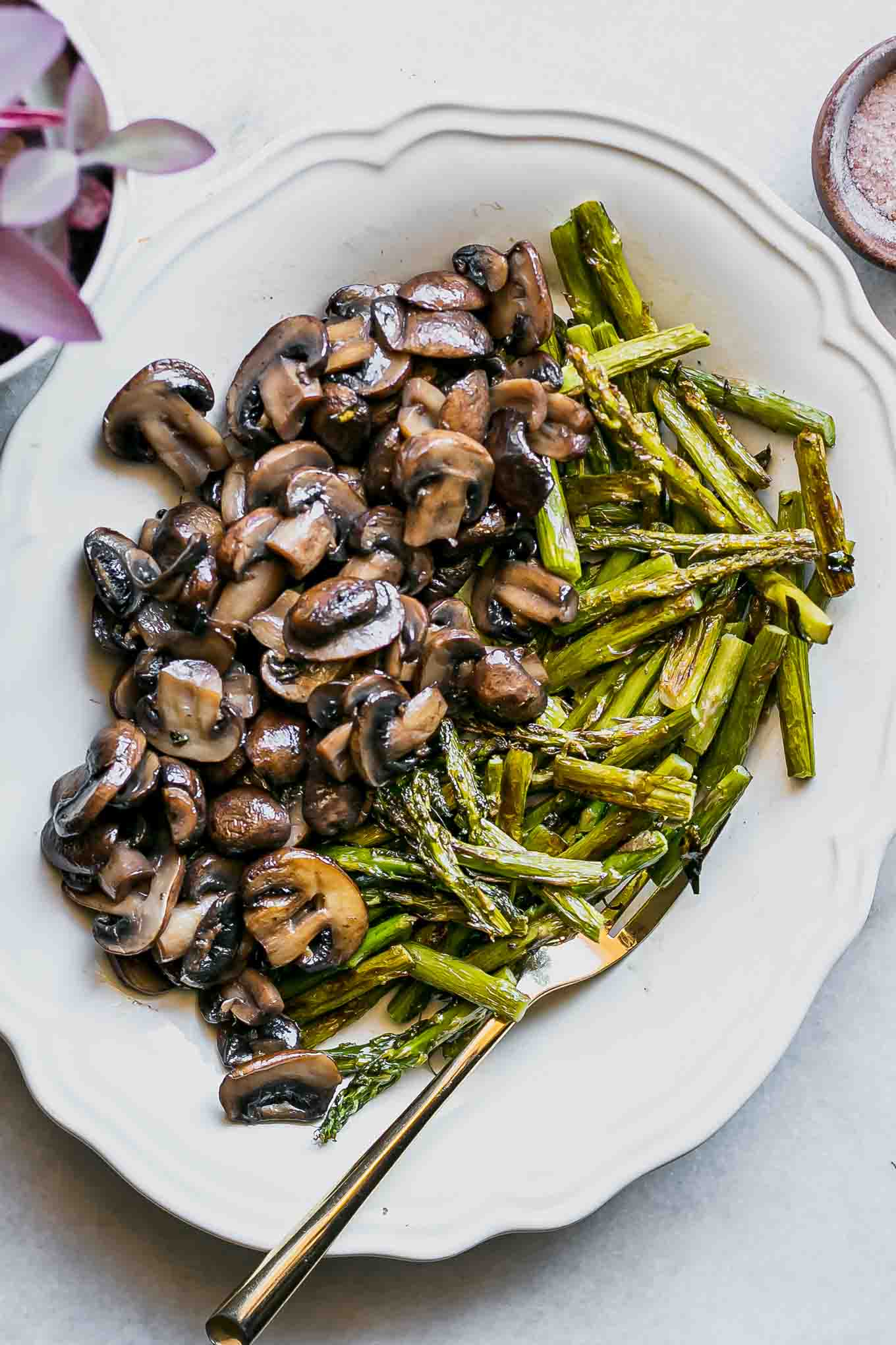 roasted mushrooms and asparagus on a white plate with a gold fork