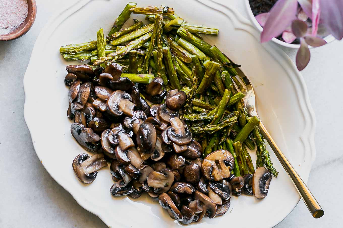 cut mushrooms and asparagus on a white plate with a gold fork