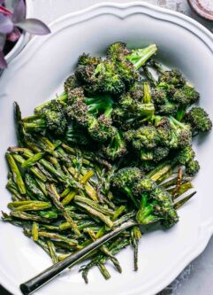 baked broccoli and asparagus on a white plate with a gold fork