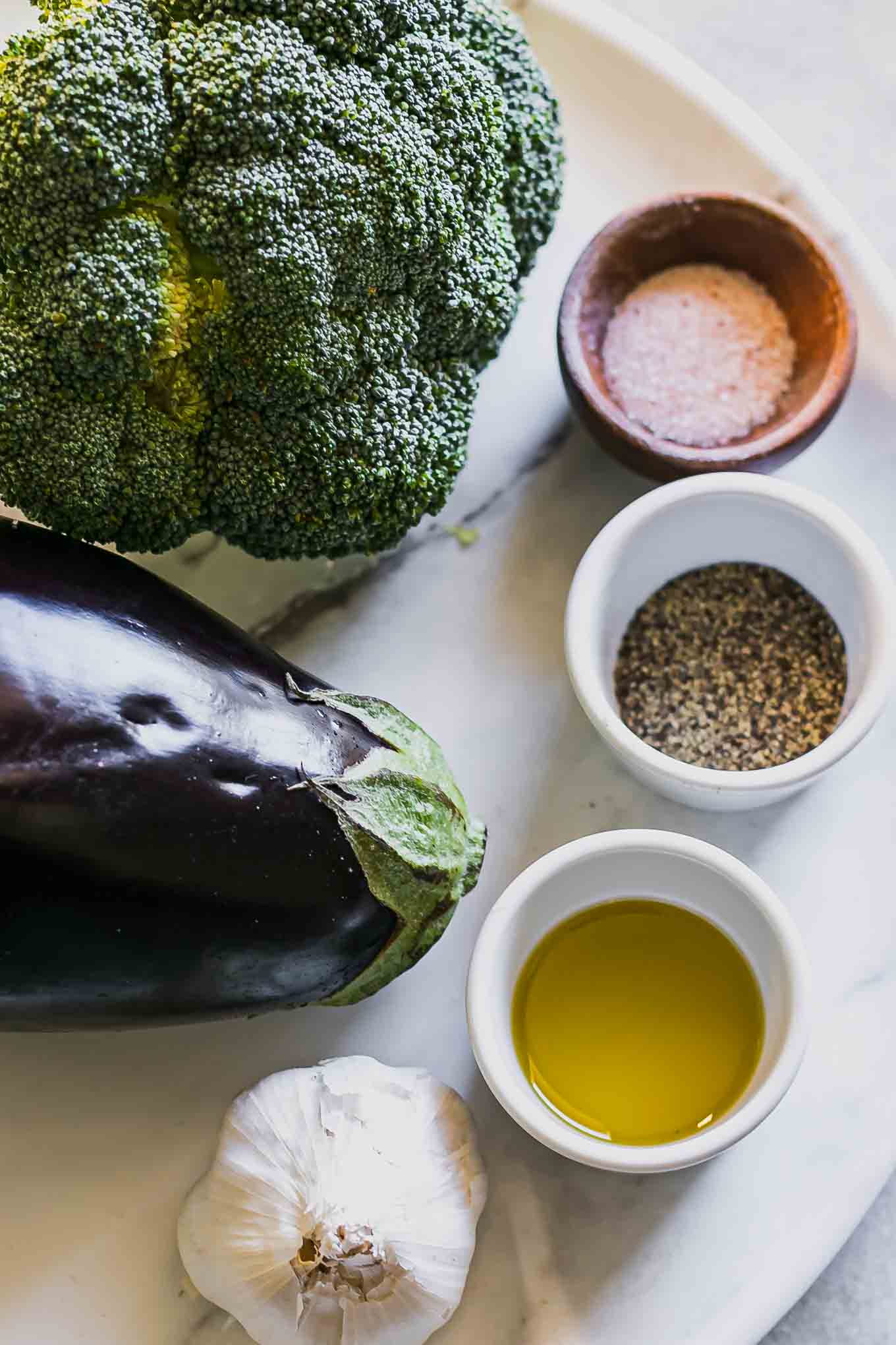 eggplant, broccoli, garlic, oil, salt, and pepper on a white table