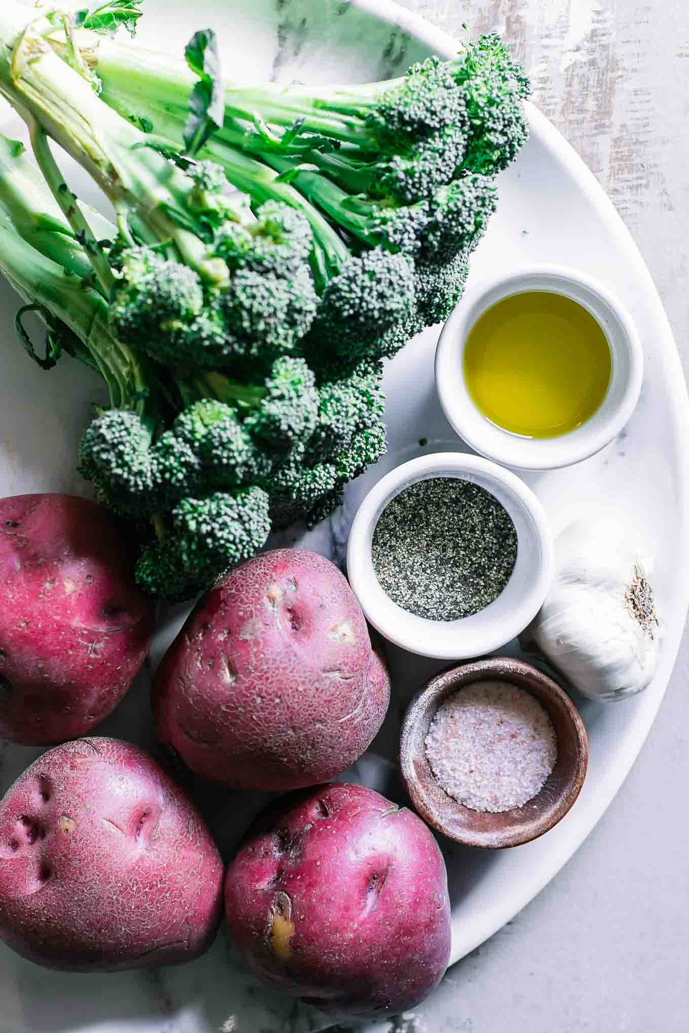 red potatoes, broccoli, garlic, salt, pepper, and oil on a white table