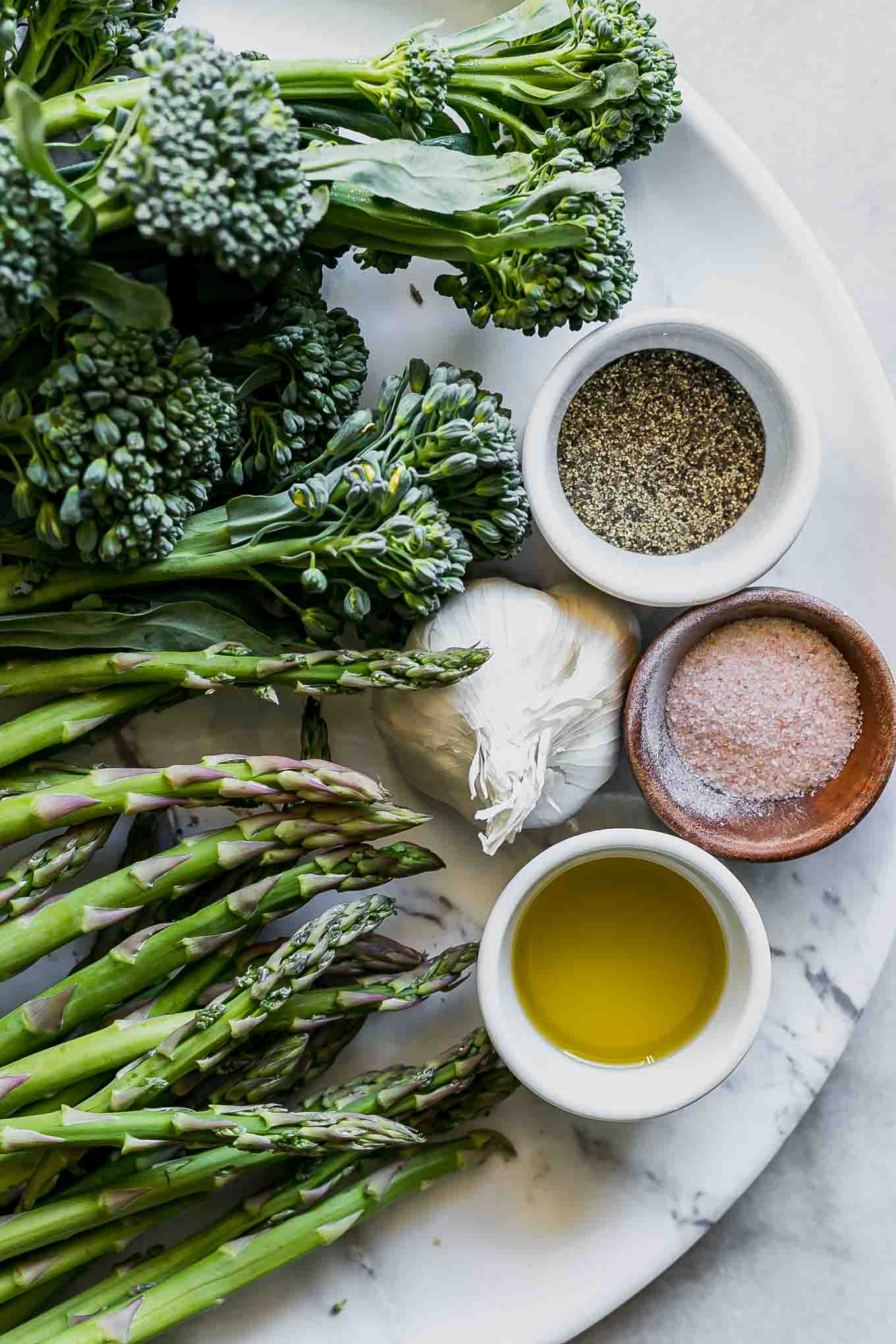 broccolini, asparagus, garlic, oil, salt, and pepper on a white table