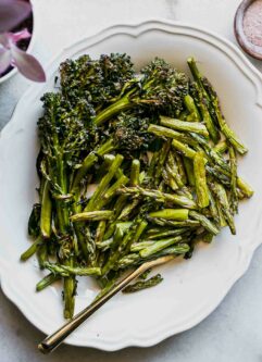 roasted asparagus and broccolini on a white plate with a gold fork
