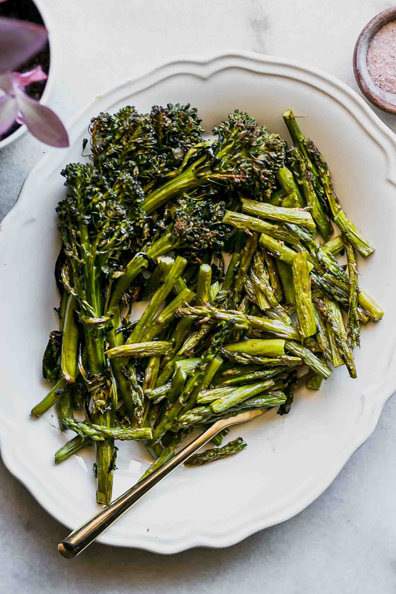roasted asparagus and broccolini on a white plate with a gold fork