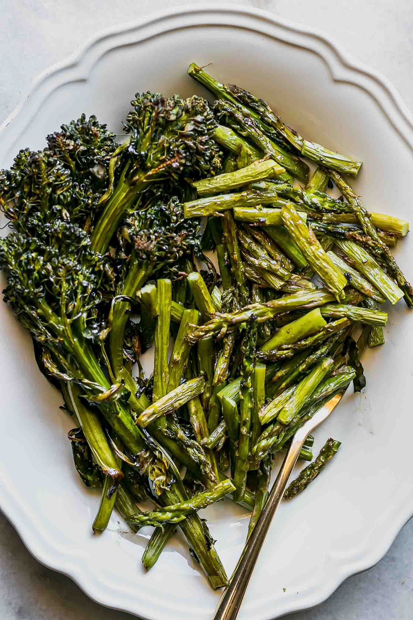 a close up photo of a white plate with roasted asparagus and broccolini