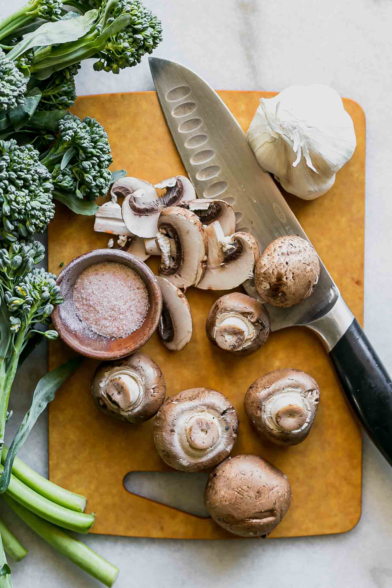 cut mushrooms and broccolini on a wood cutting board
