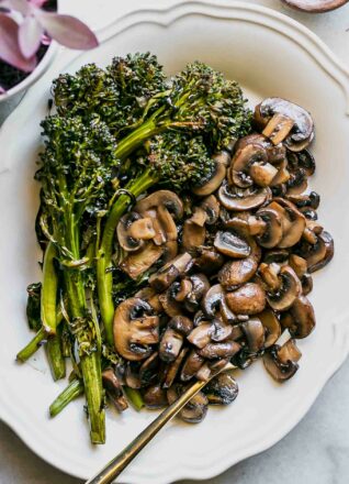 roasted mushrooms and broccolini on a white plate with a gold fork