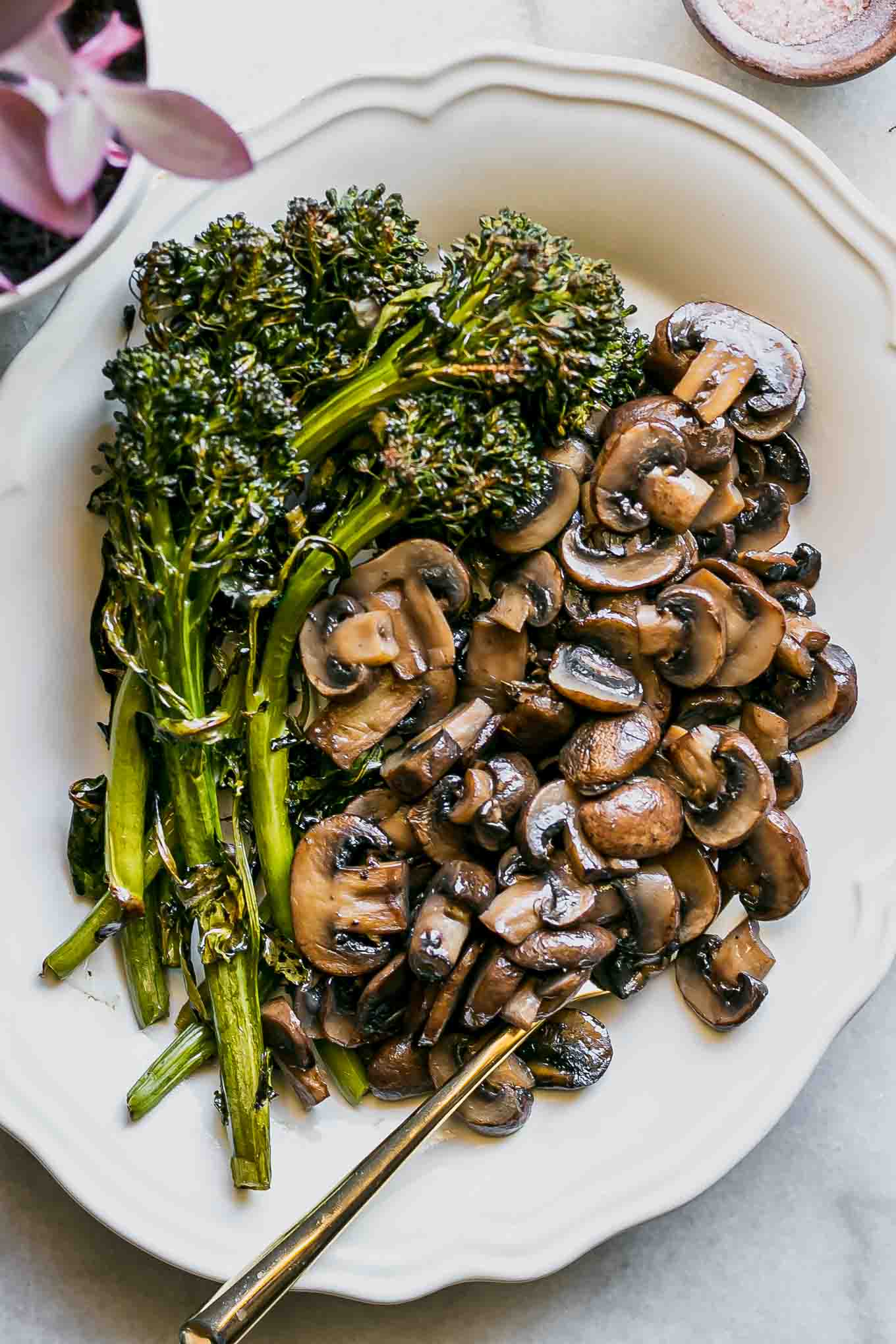 roasted mushrooms and broccolini on a white plate with a gold fork