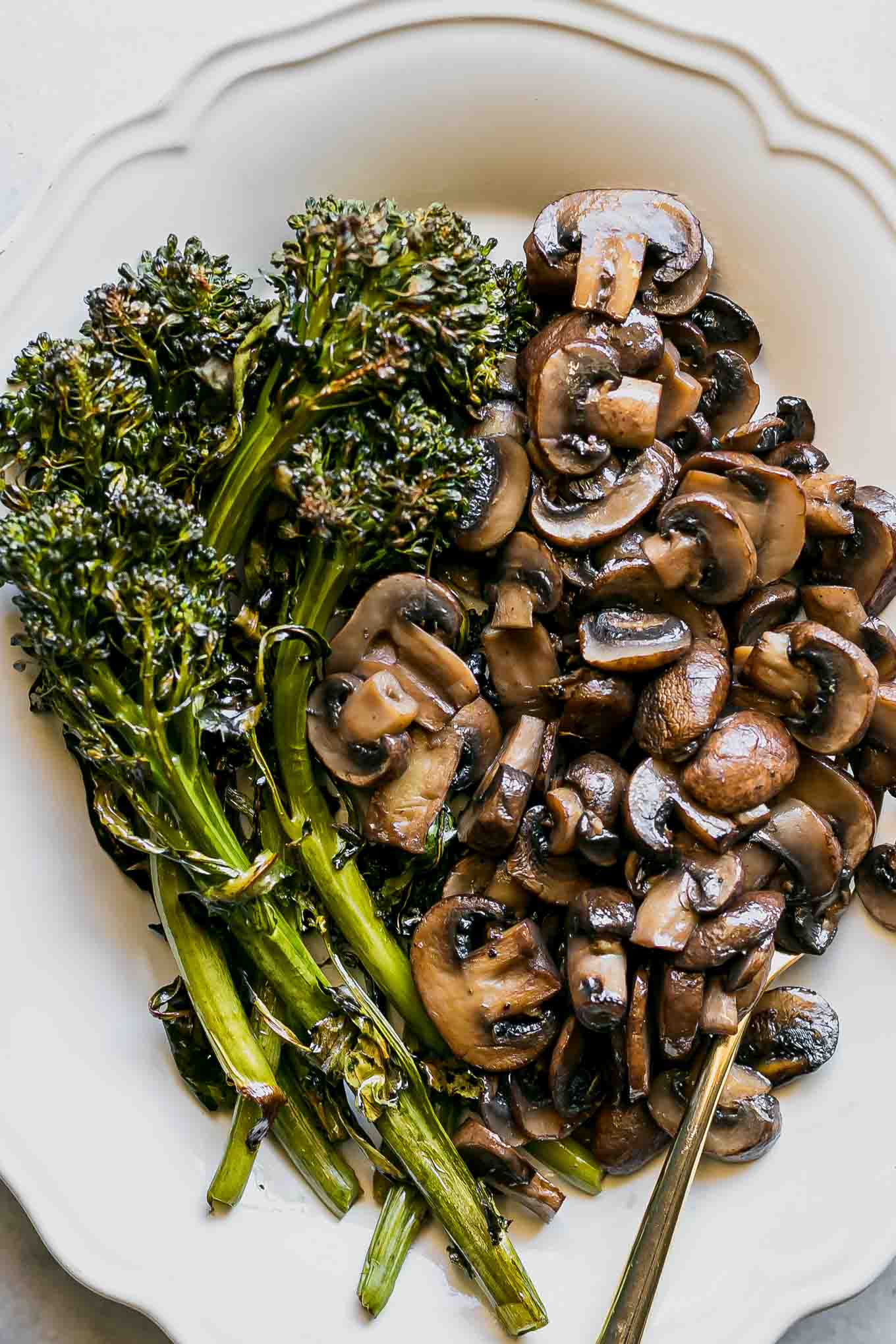 a close up photo of baked broccolini and mushrooms on a side dish