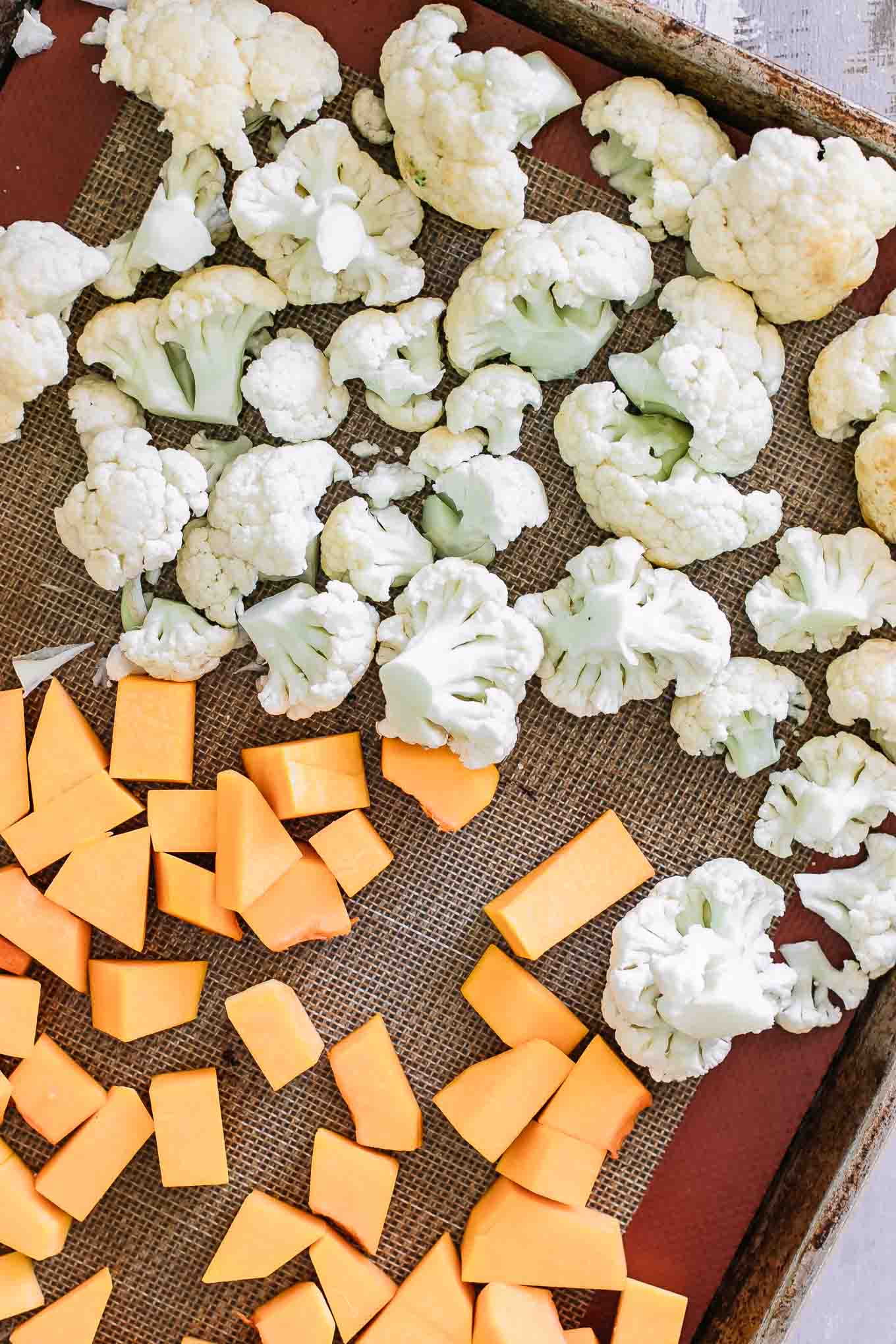 cut butternut squash and cauliflower florets on a baking sheet before roasting