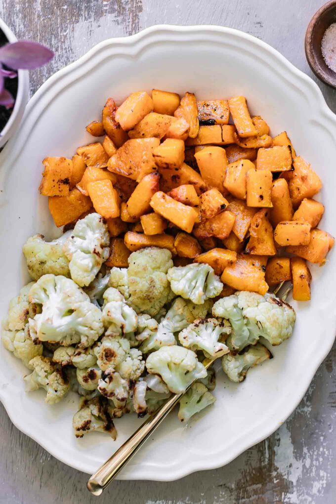 roasted cauliflower and butternut squash on a white plate with a gold fork