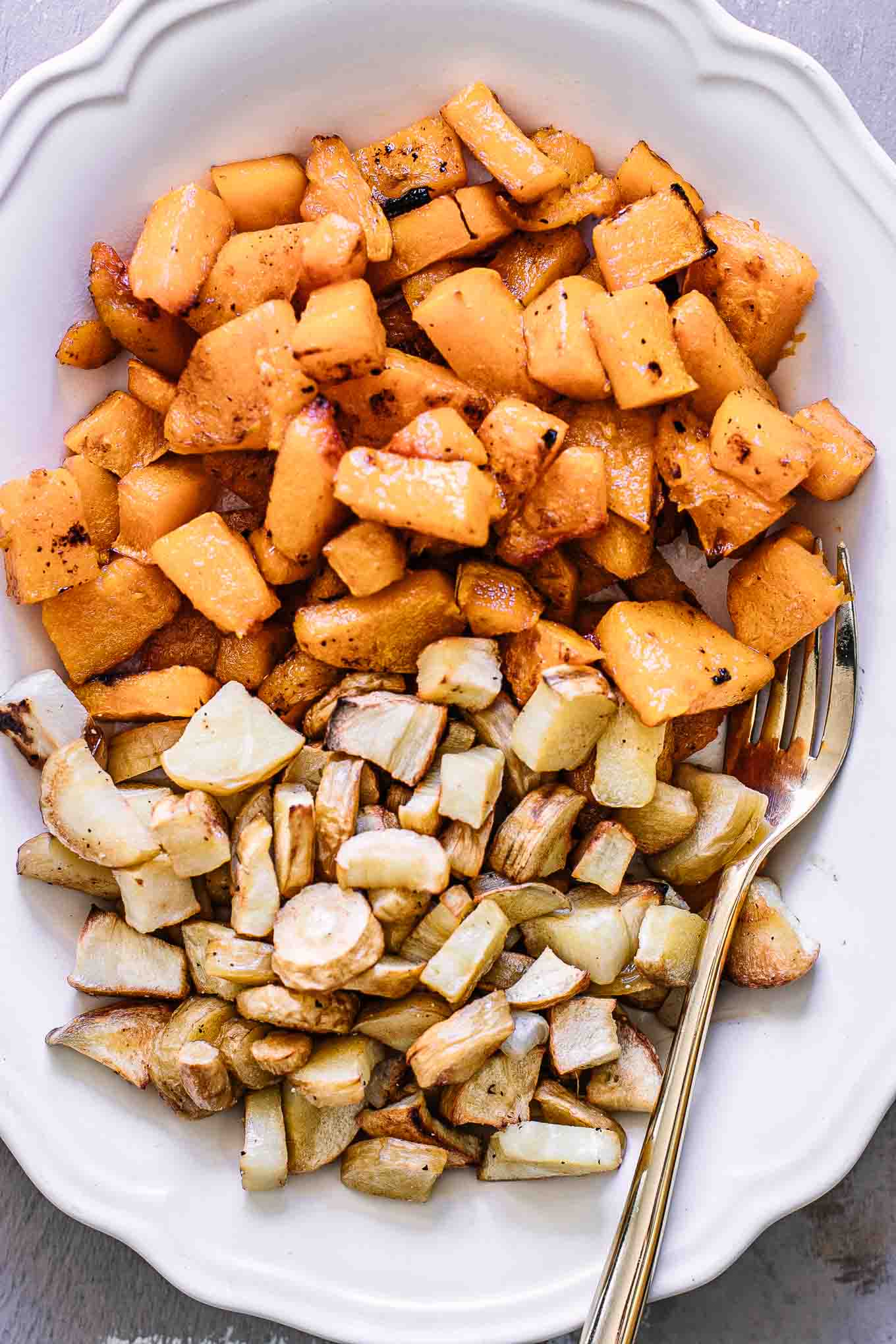 a close up photo of baked butternut squash and parsnips on a white serving dish