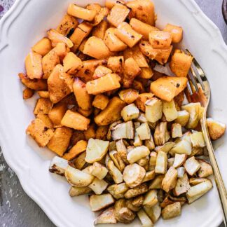 a white side dish with roasted butternut squash and parsnips and a gold fork