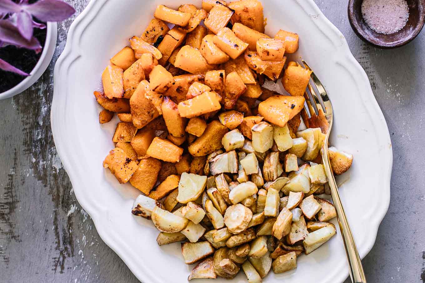 a white side dish with roasted butternut squash and parsnips and a gold fork