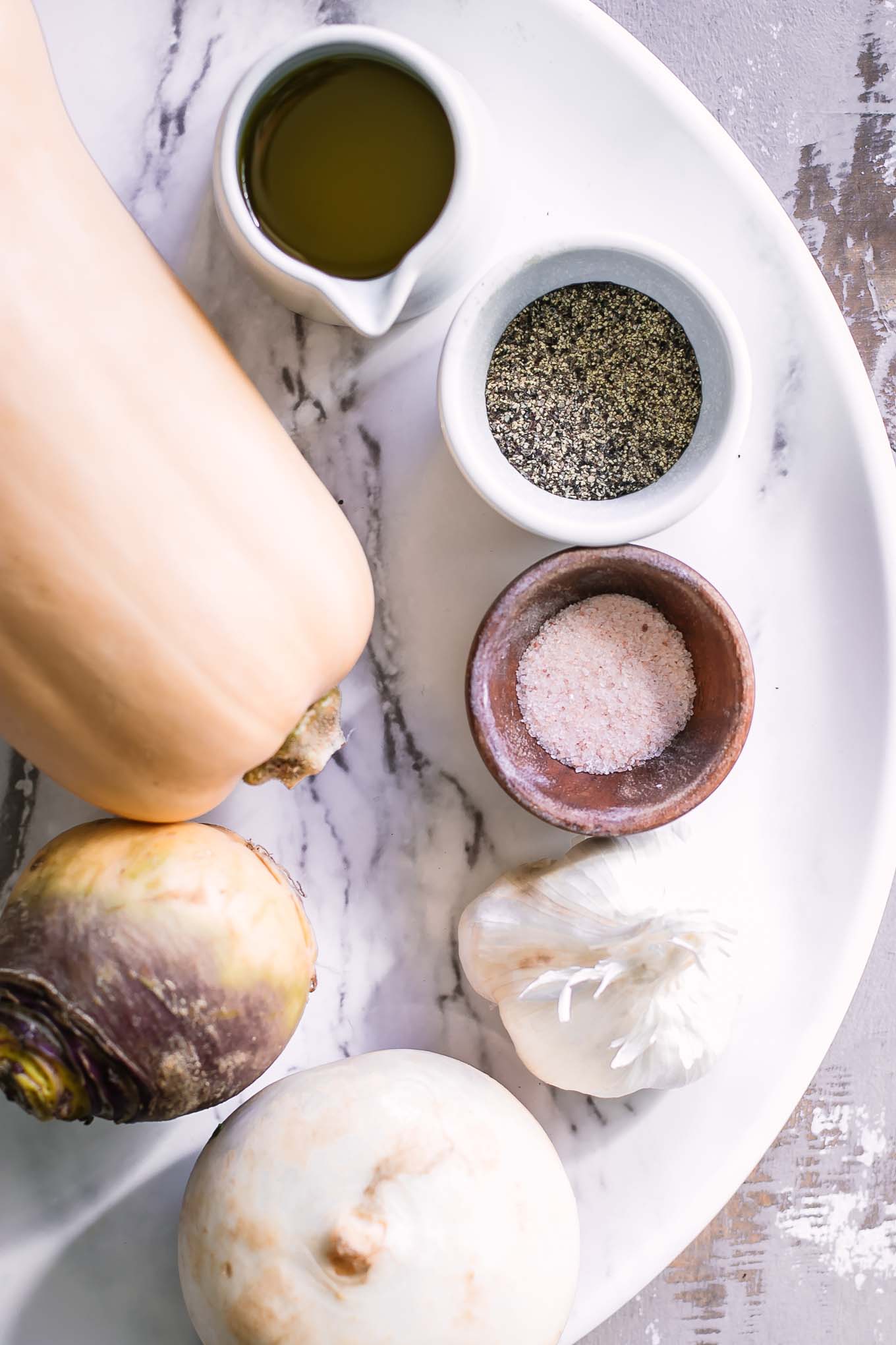 butternut squash, turnips, garlic, oil, salt, and pepper on a table