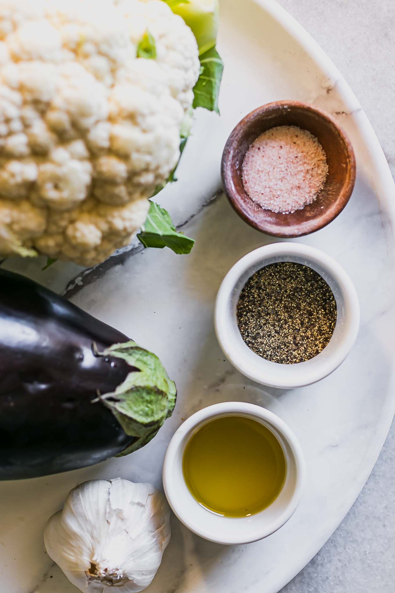 cauliflower, eggplant, garlic, and bowls of oil, salt, and pepper on a white table