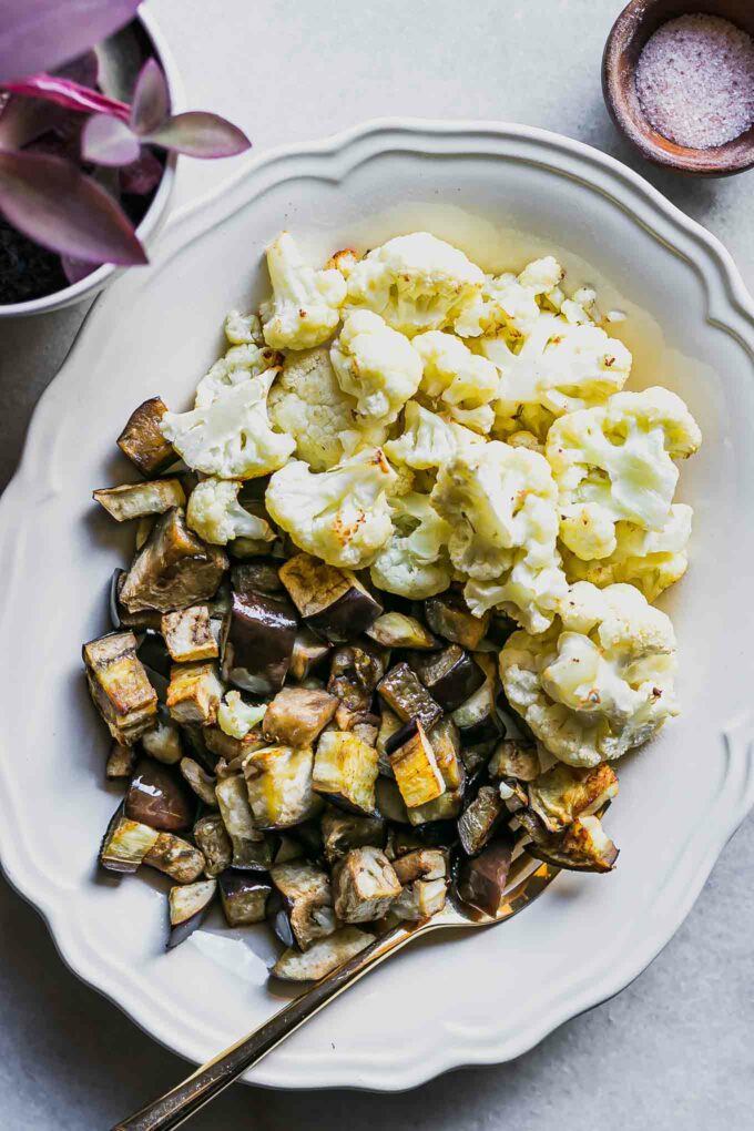 roasted cauliflower and eggplant on a white table with a gold fork