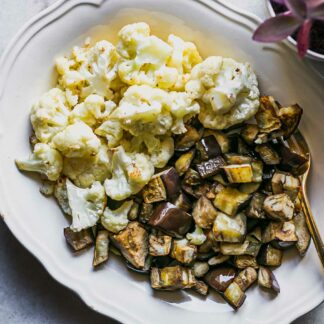 a white side dish with baked cauliflower and eggplant on a white table
