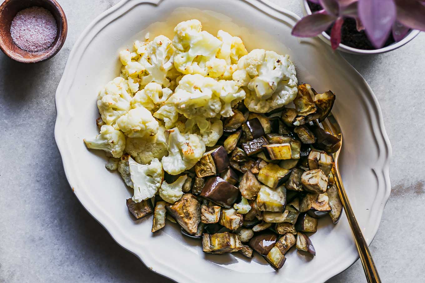 a white side dish with baked cauliflower and eggplant on a white table