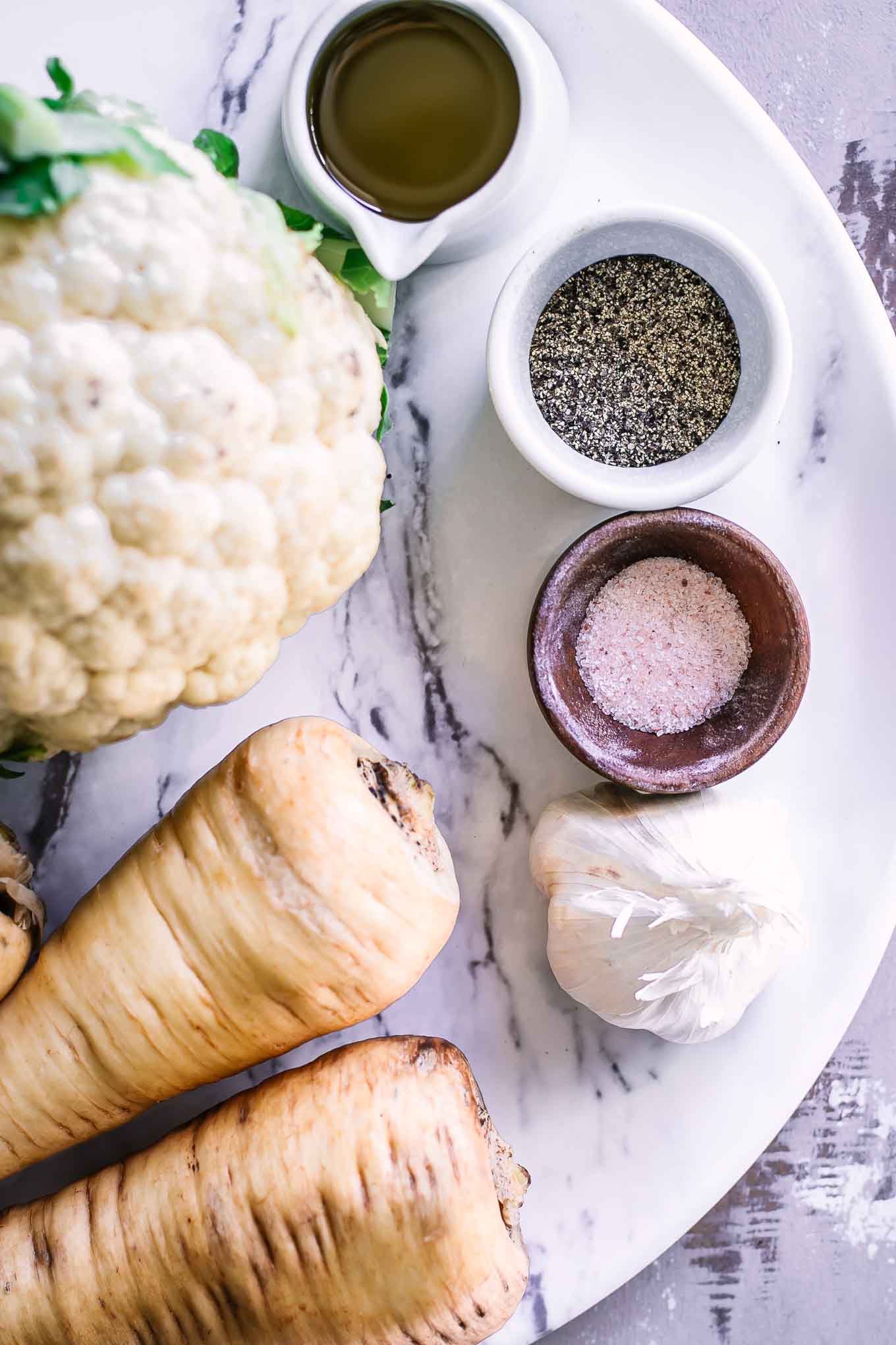 cauliflower, parsnips, garlic, oil, salt, and pepper on a white table