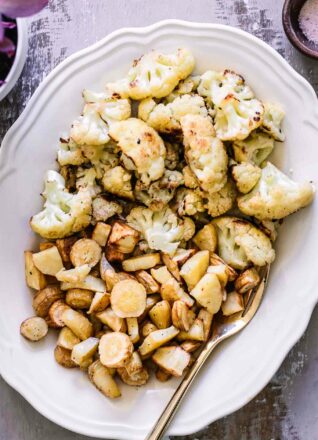 baked parsnips and cauliflower on a white plate with a gold fork