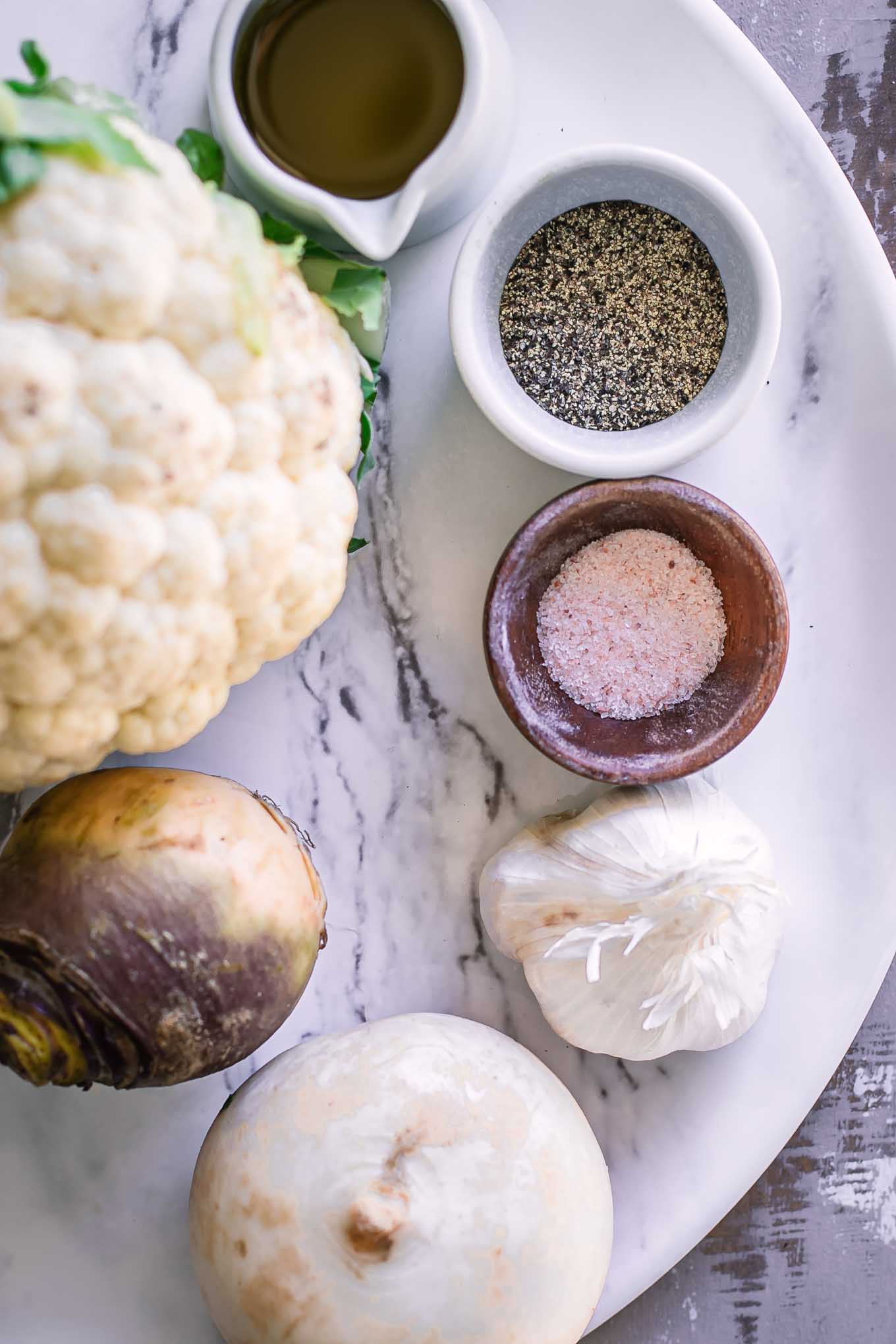 cauliflower, turnips, garlic, oil, salt, and pepper on a white table