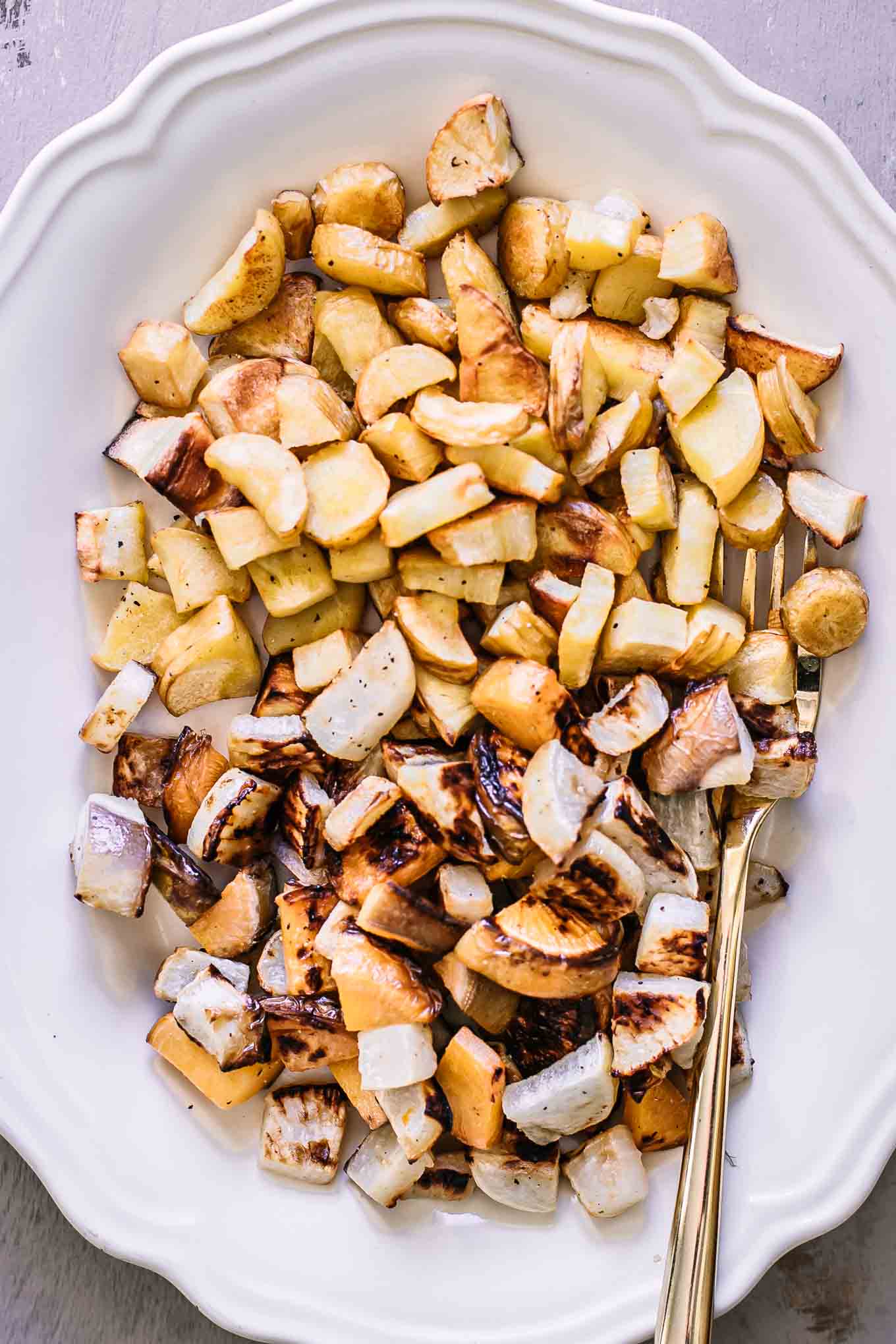 a close up photo of roasted turnips and parsnips on a white plate
