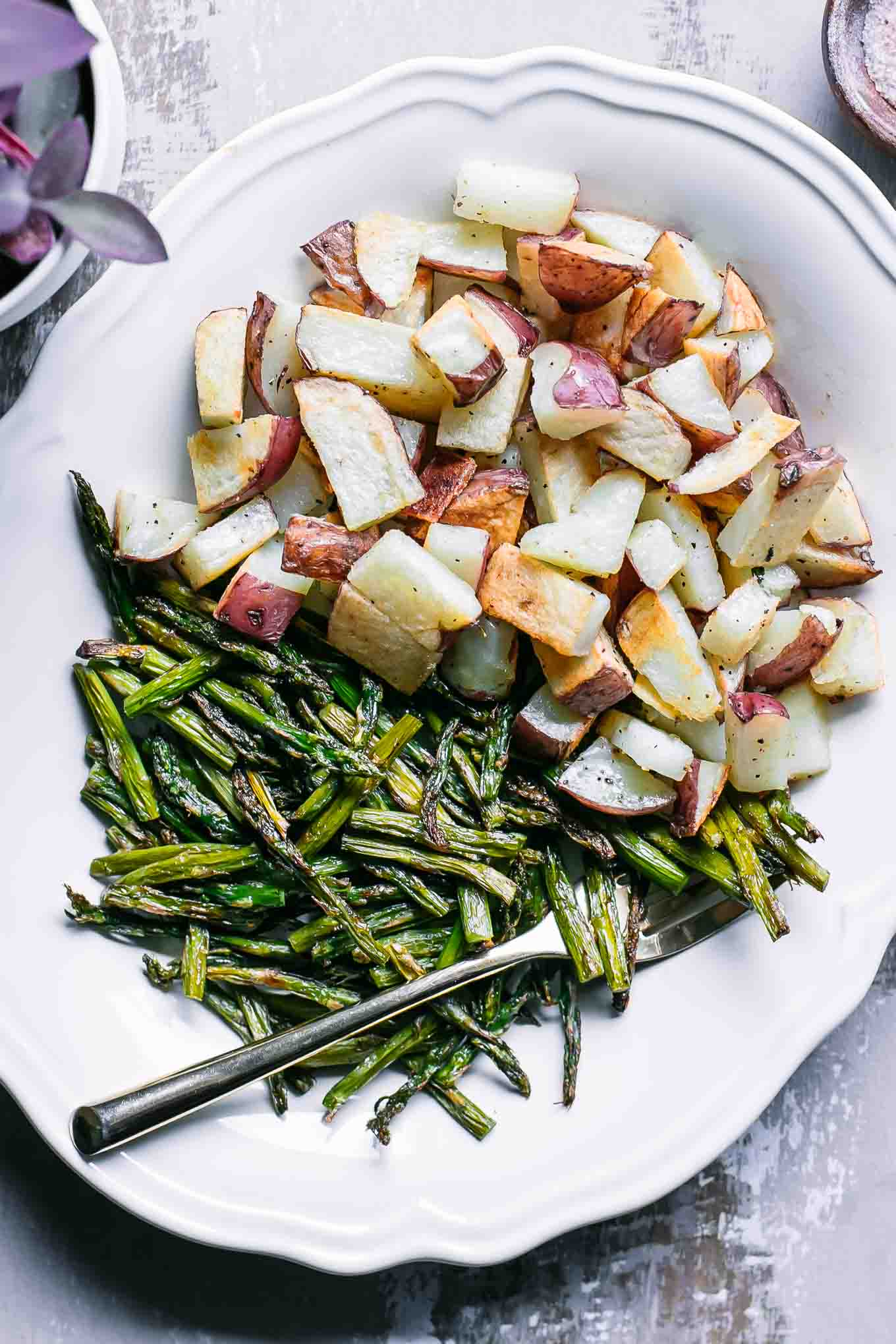 a white plate with roasted potatoes and asparagus and a gold fork