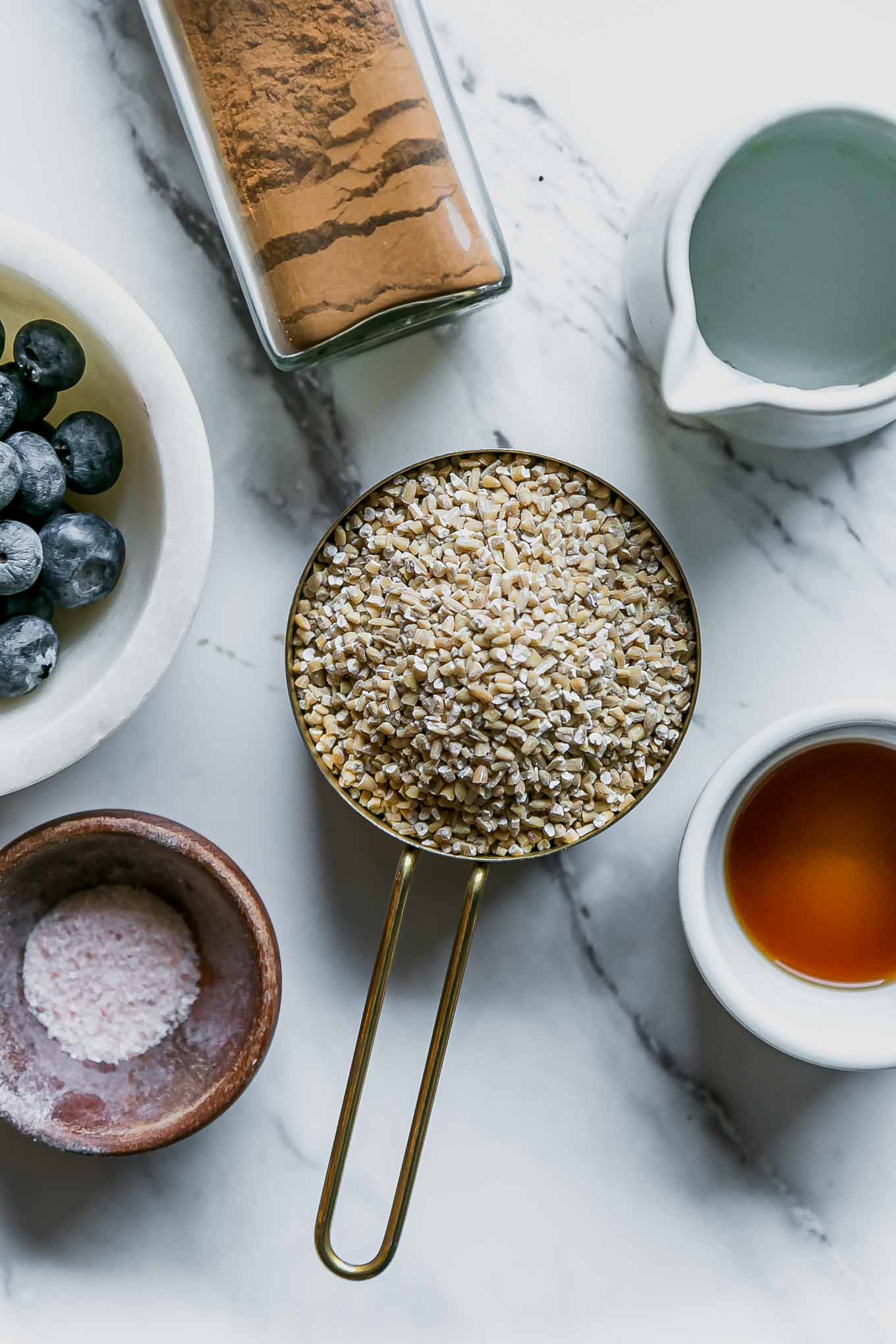 bowls of oatmeal, blueberries, cinnamon, vanilla, maple syrup, and water on a white table