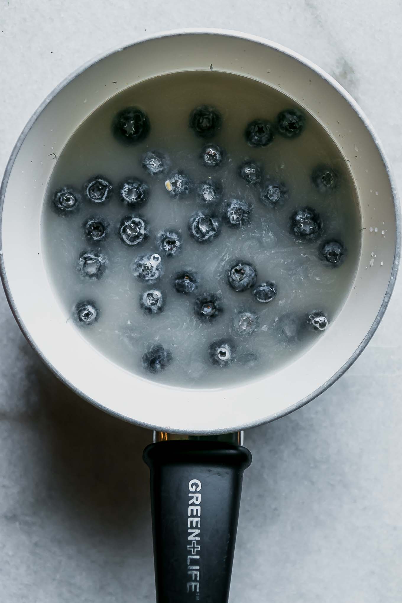 a small white pot with oatmeal, blueberries, and water on a white table