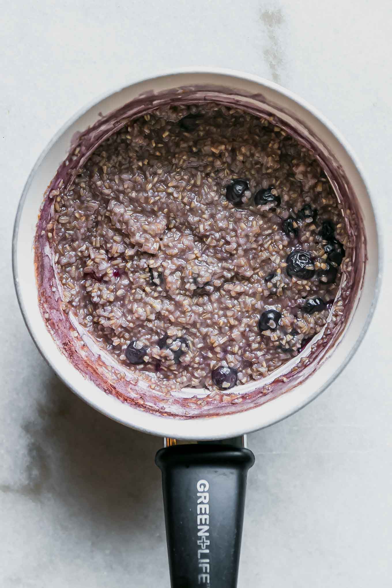 a small pot with cooked blueberry oatmeal on a white table