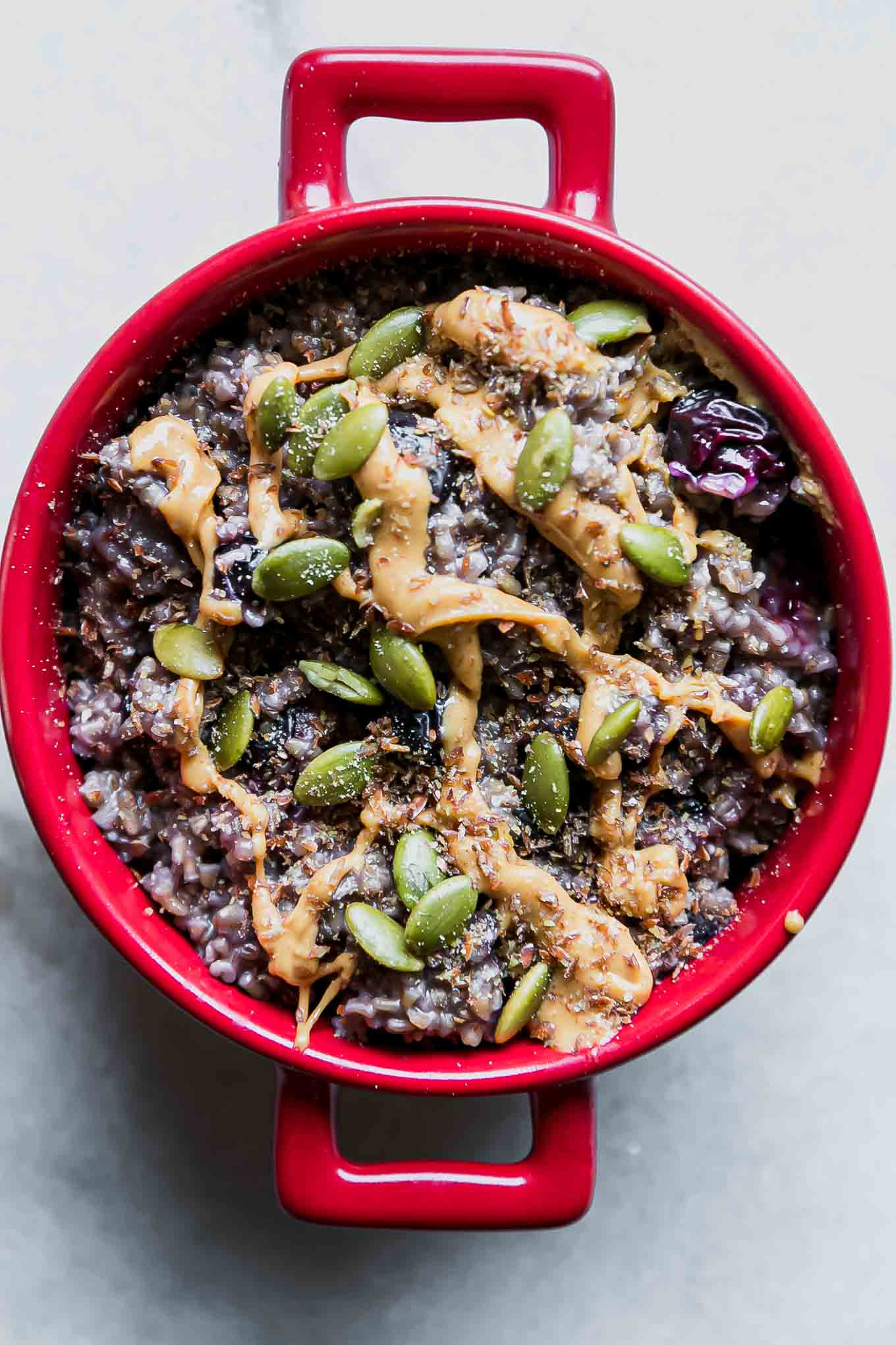 a close up photo of blueberry oatmeal in a red bowl on a white table