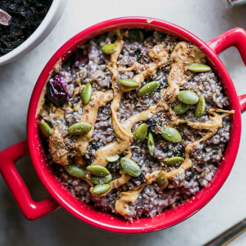 a bowl of blueberry oatmeal with drizzled nut butter and seeds on top
