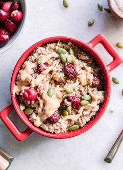 a red bowl of cranberry oatmeal on a white table with a bowl of fresh cranberries