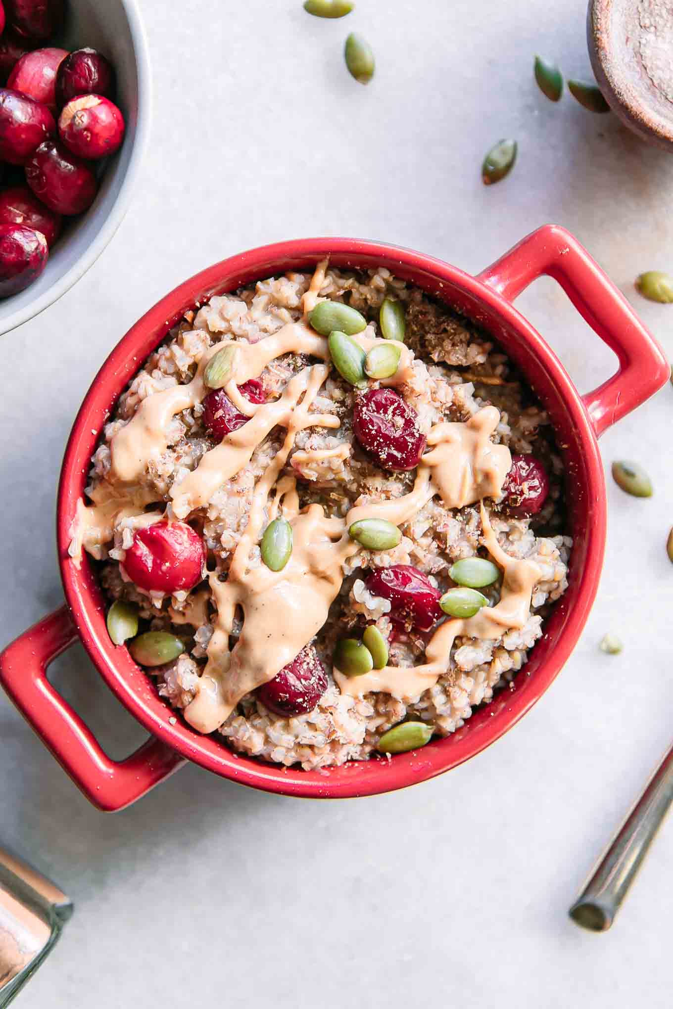 a red bowl of cranberry oatmeal on a white table with a bowl of fresh cranberries