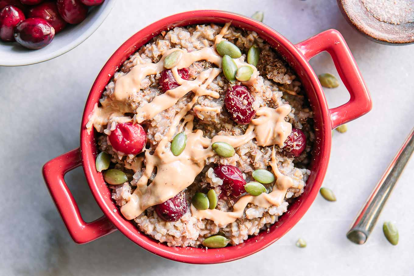 a red bowl of cranberry oatmeal with a gold fork on a white table