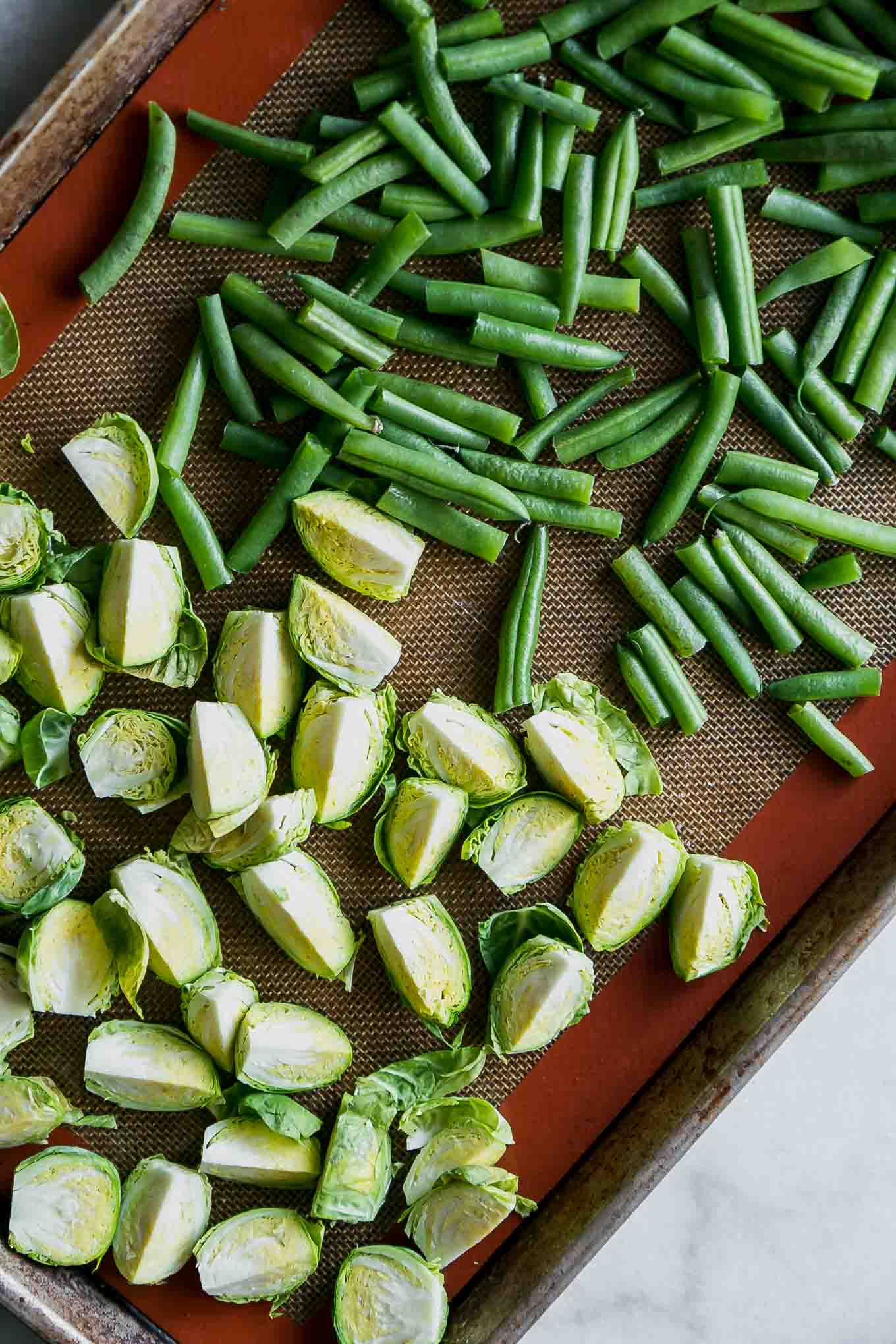 cut brussels sprouts and green beans on a baking sheet before roasting