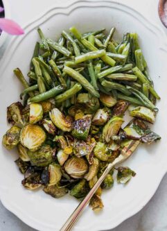 roasted green beans and brussels sprouts on a white plate with a gold fork