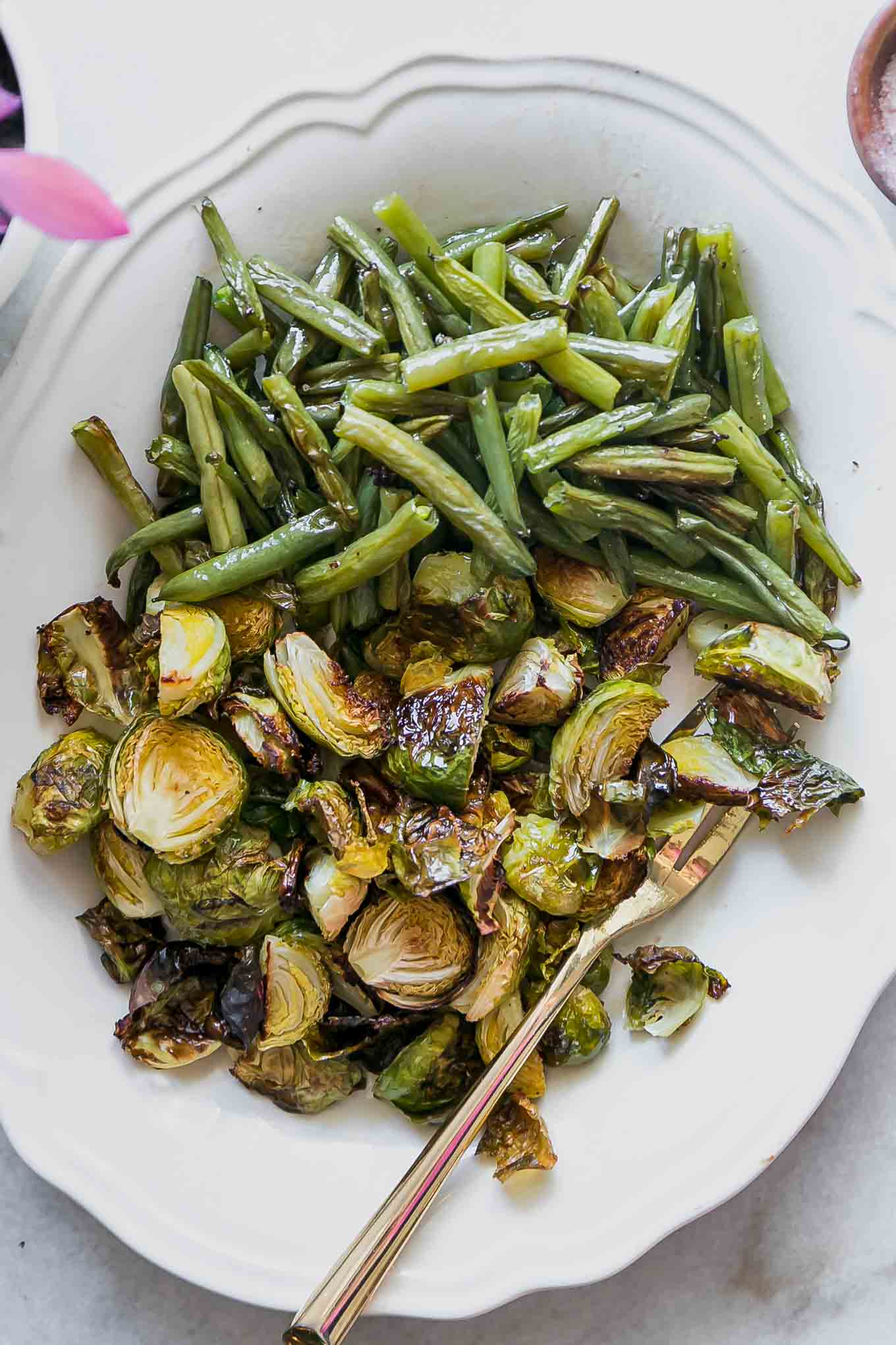 roasted green beans and brussels sprouts on a white plate with a gold fork