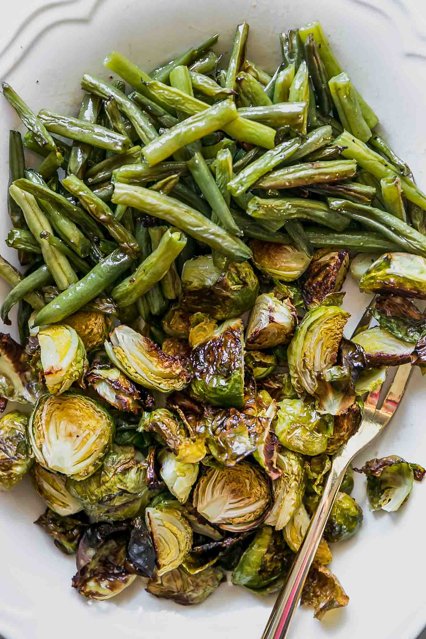a close up photo of baked green beans and brussels sprouts on a white plate