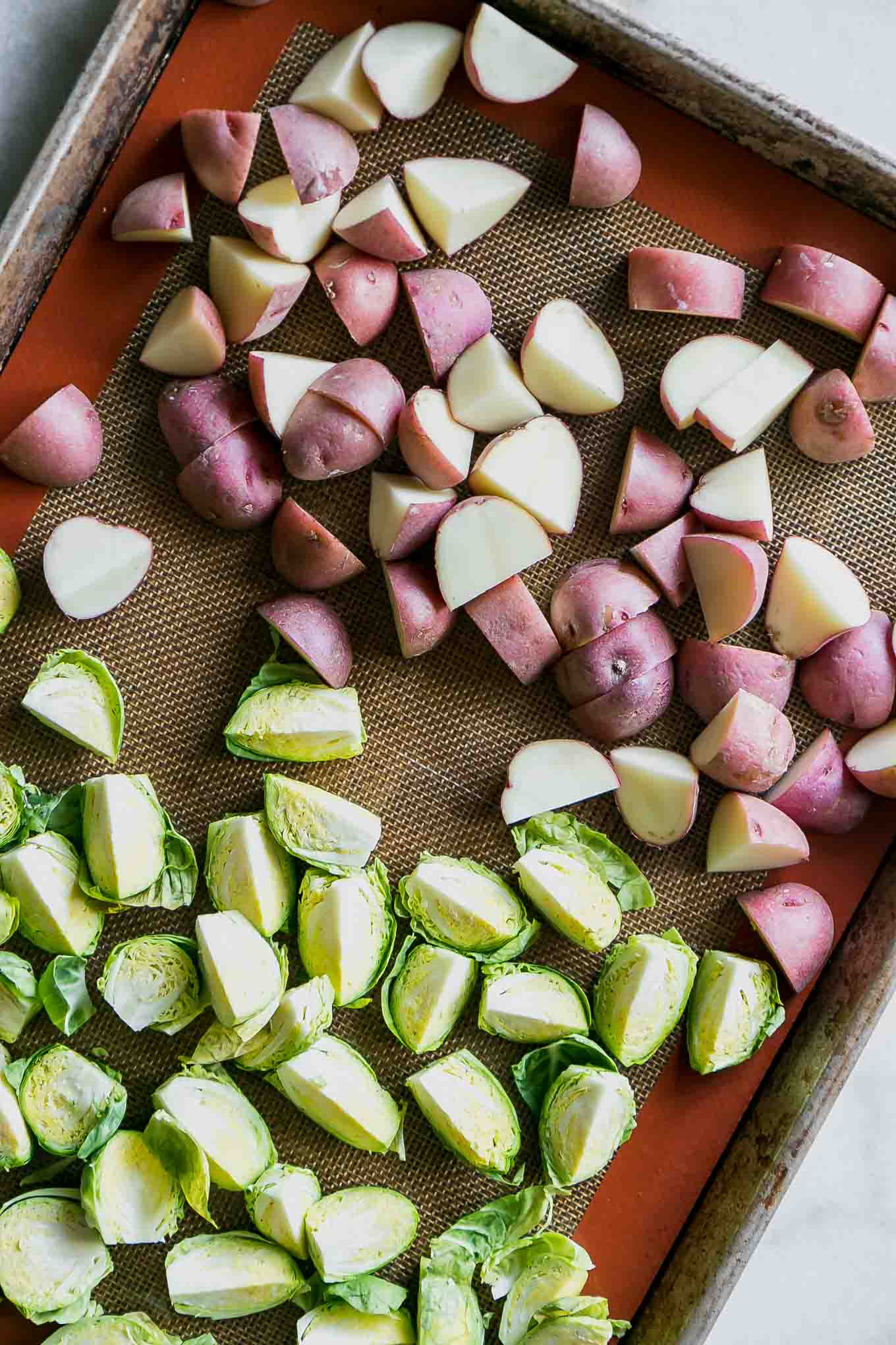 cut brussels sprouts and potatoes on a baking sheet before roasting