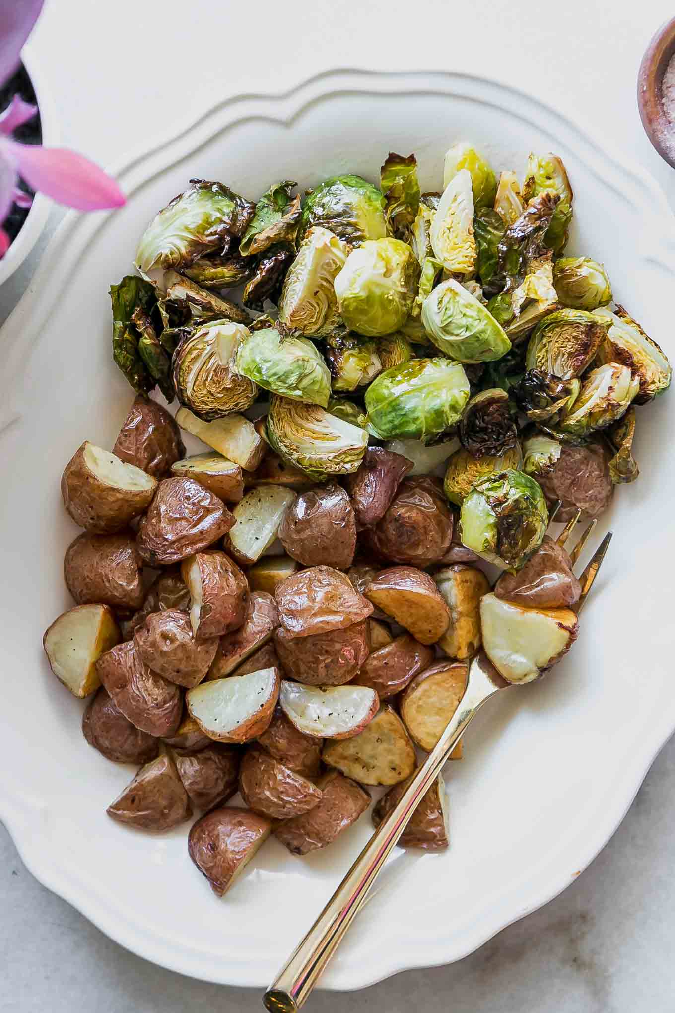 baked potatoes and brussels sprouts on a white plate with a gold fork