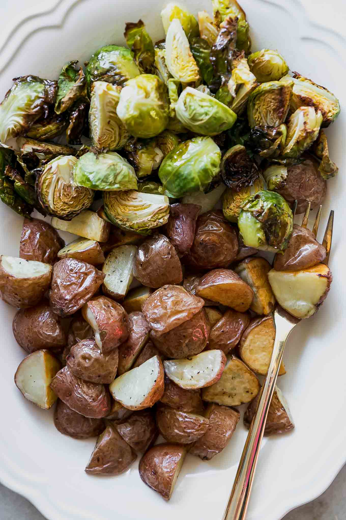 a close up photo of brussels sprouts and potatoes on a white plate