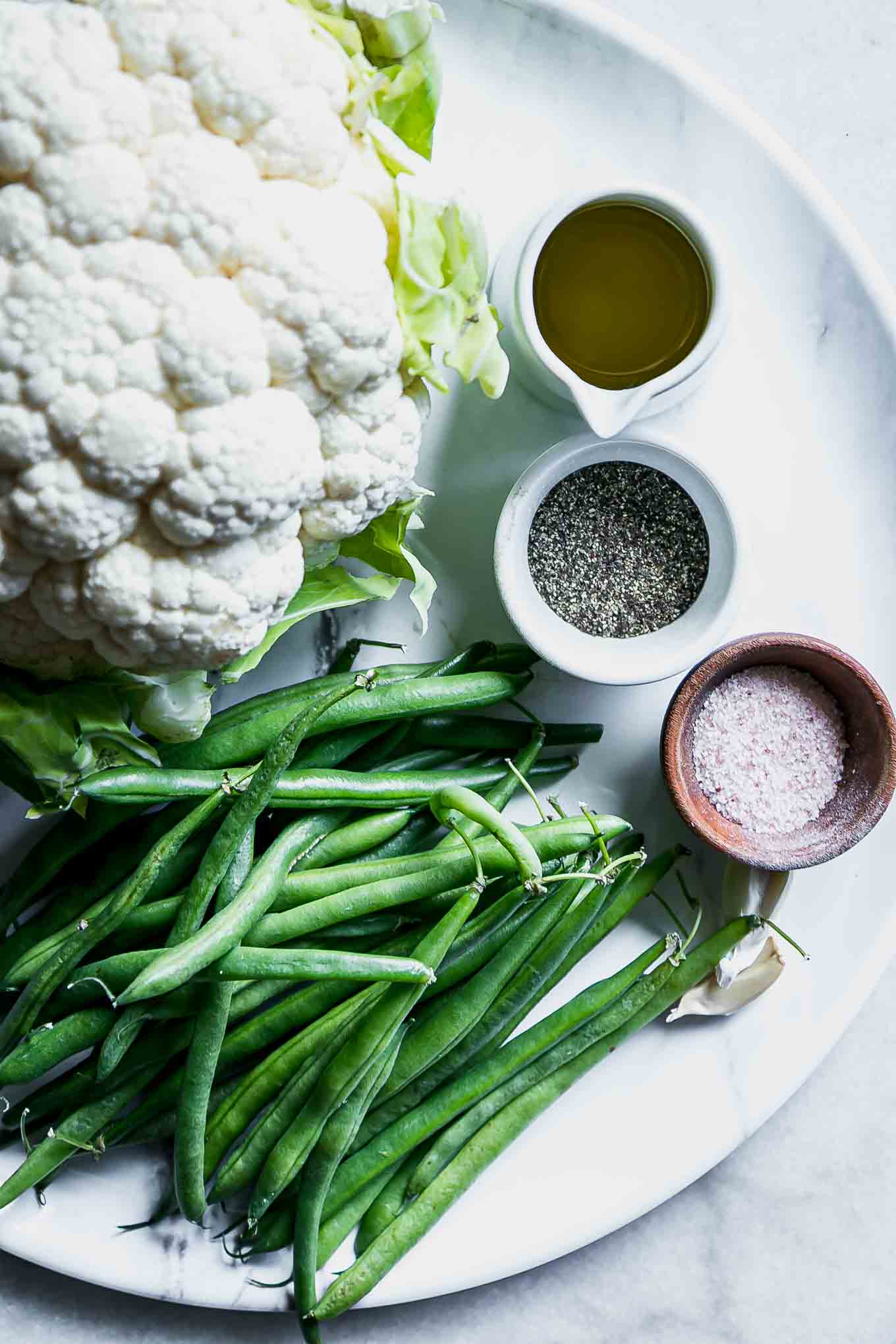 cauliflower, green beans, garlic, oil, salt, and pepper on a white table