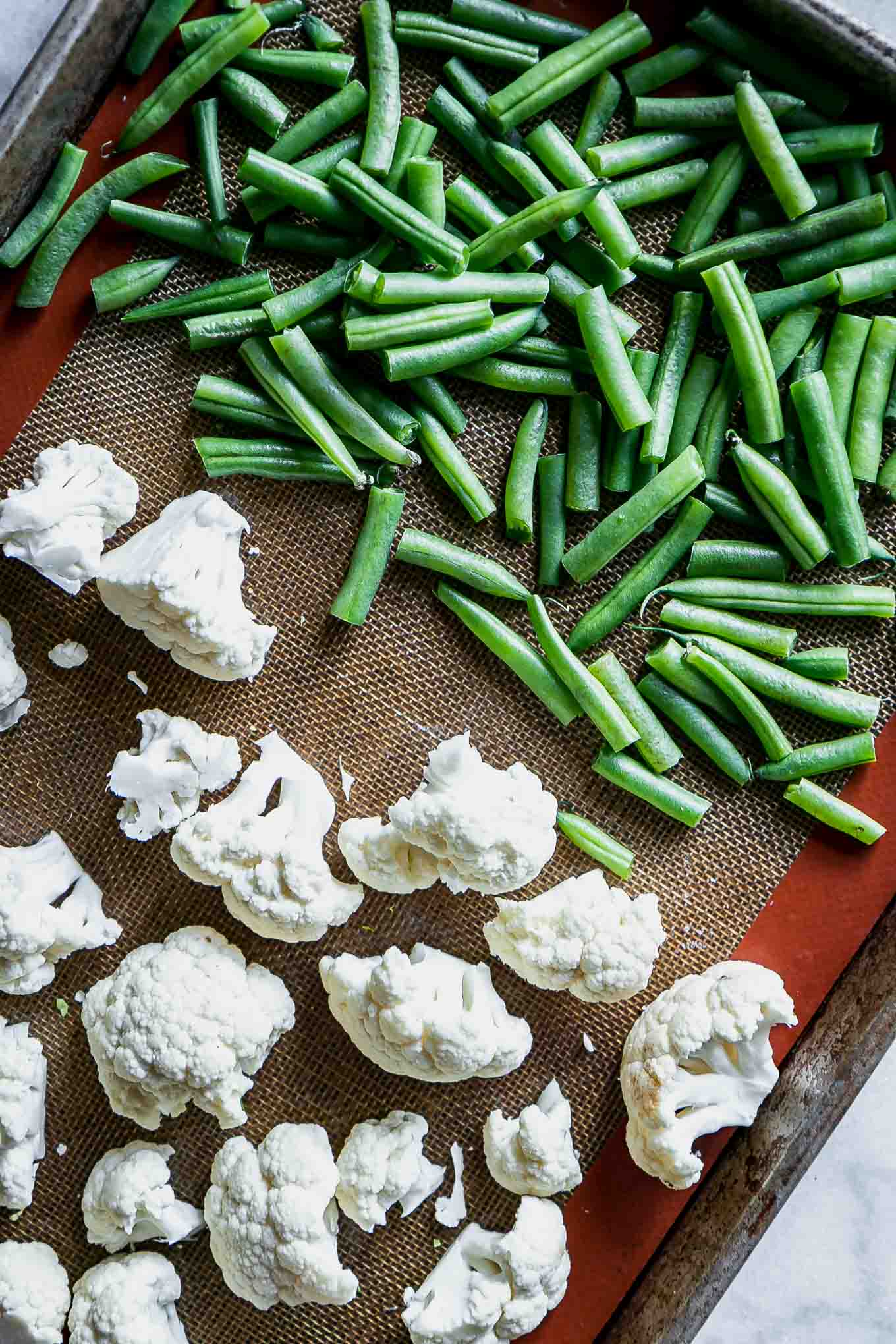 cut cauliflower and green beans on a baking sheet before roasting