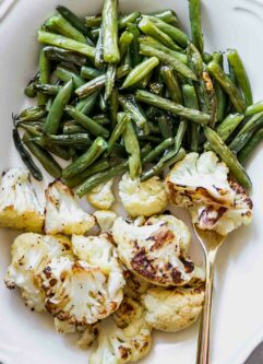 a close up photo of roasted green beans and cauliflower on a white plate