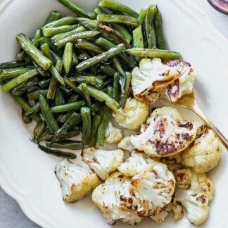 baked green beans and cauliflower on a white side dish plate