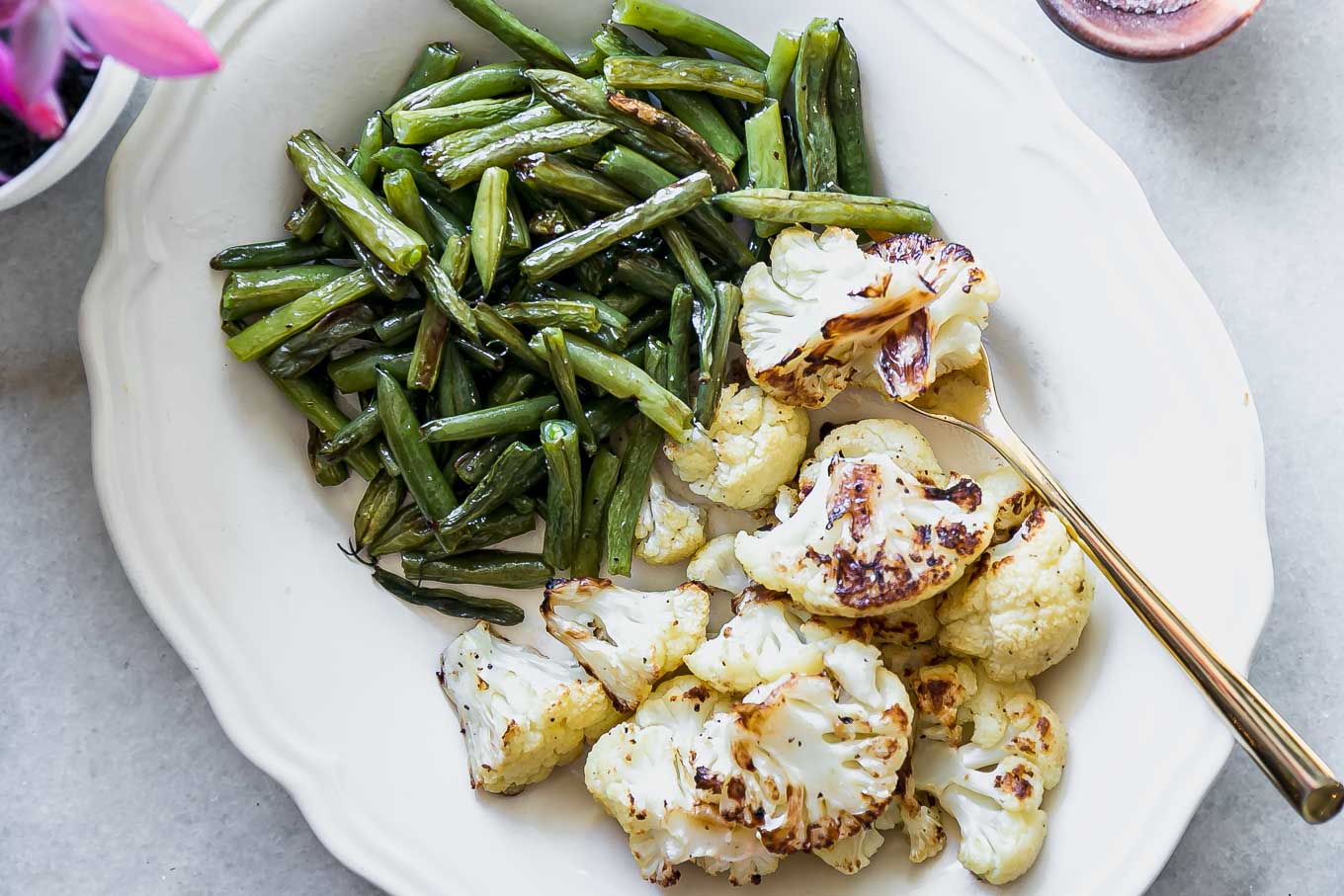 baked green beans and cauliflower on a white side dish plate