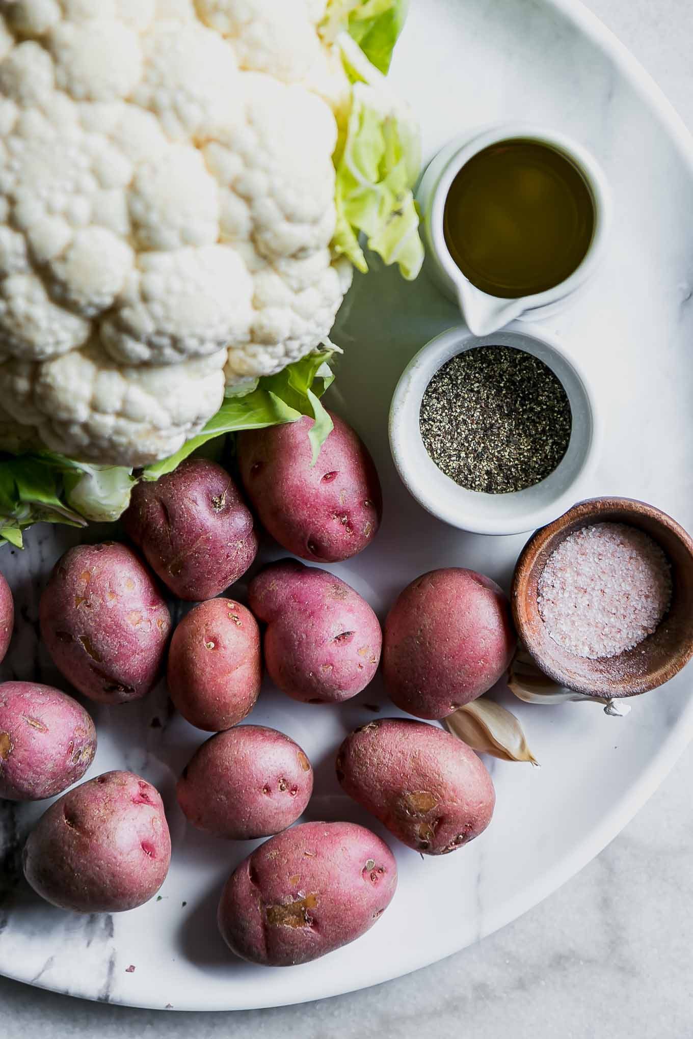 cauliflower, potatoes, garlic, oil, salt and pepper on a white table