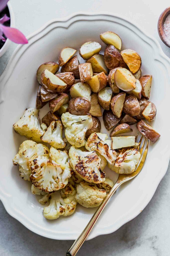 baked cauliflower and potatoes on a white side dish with gold forks